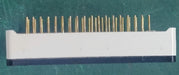 A white rectangular electronic component with multiple vertical gold pins on top, resting on a textured green surface.