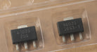 A close-up of a small electronic component in a clear plastic carrier tray, resting on a speckled gray countertop. The component has a black body with white printed text reading 'A803G' and '25C2-1'.