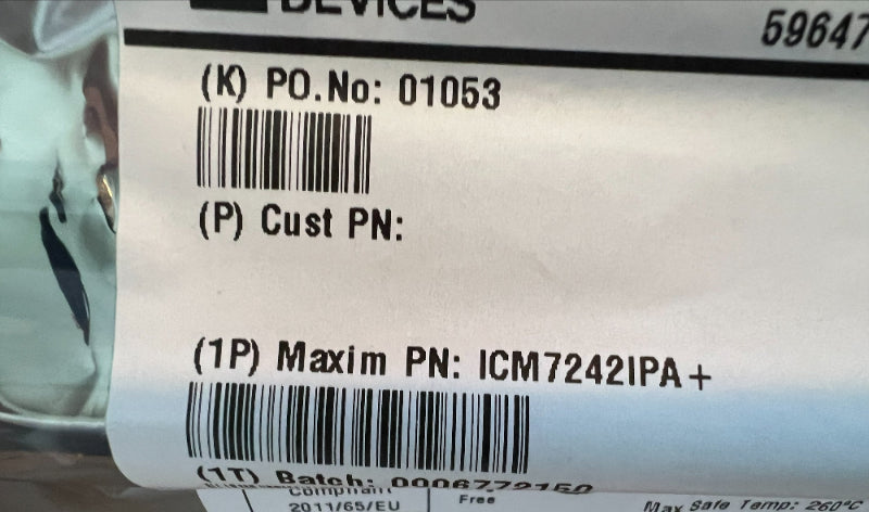 A close-up of a white product label with black printed text and barcodes, placed on a wooden surface next to a metallic object. The label includes product identifiers such as P.